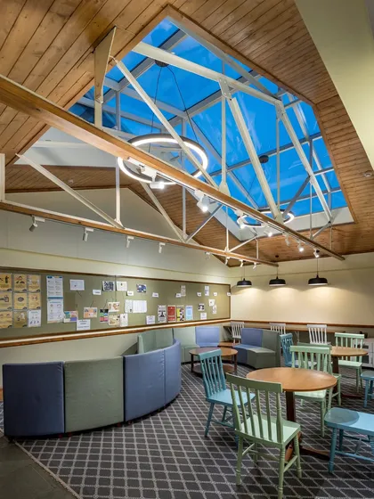Another view of the student lounge, showing how we use curved, modular furniture to create flexible social spaces under the dramatic skylight and exposed trusses.
