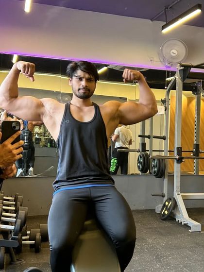 Full view of the seated double bicep pose in the gym environment.