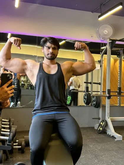 Full view of the seated double bicep pose in the gym environment.