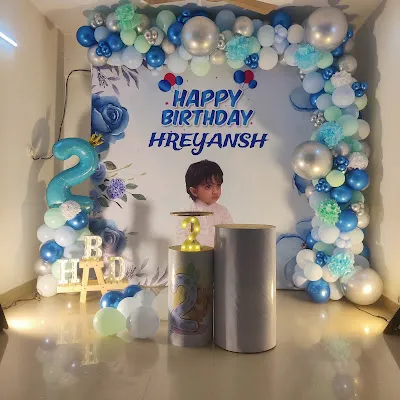 A blue and silver themed decoration for a second birthday. This setup includes a personalized backdrop with the child's photo and a beautiful balloon arch.