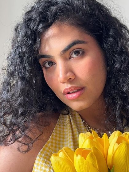 Posing with fake flowers until someone gives me real ones. A close-up selfie with yellow tulips, my yellow gingham top, and a playful caption.