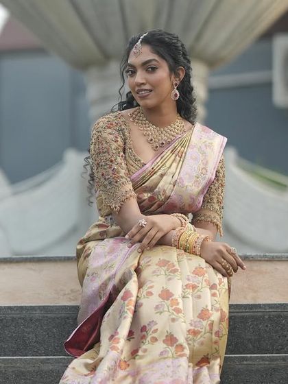 A full length view of the bride seated, showing the flow and richness of her floral silk saree. The custom blouse sparkles, tying the entire traditional look together with a touch of modern craftsmanship.