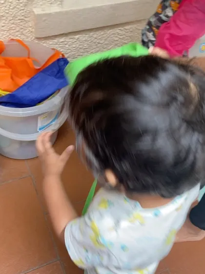Close-up of a toddler participating in clean-up time. Every child is encouraged to help, fostering a sense of teamwork and shared responsibility in the classroom.