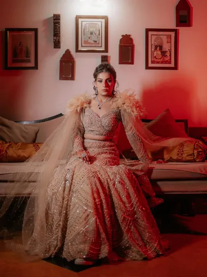 A regal portrait of the bride, Rozy, seated on a couch during her sangeet. The dramatic red lighting and her elegant pose give the image a powerful, royal feel.