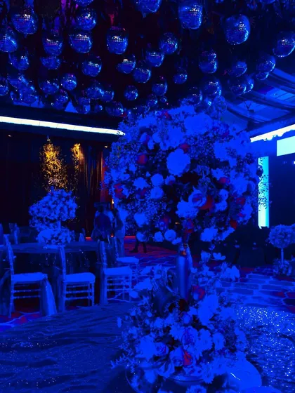 A view from the dance floor of a high-energy sangeet. The ceiling is covered in mirror disco balls, reflecting the deep blue ambient lighting and setting the perfect mood for a rave-themed party.