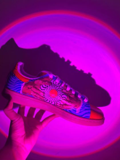 Holding up the trippy Stan Smiths under a purple light. The design is a mix of mountain silhouettes and psychedelic patterns.