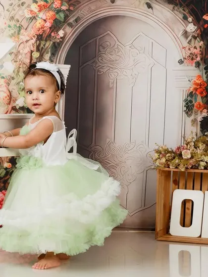 A one-year-old girl in a lovely green dress, standing at her mini piano in our floral-themed studio.