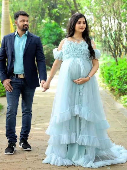 A couple walks hand-in-hand, showcasing the beautiful flow of this light blue ruffled maternity gown. It's a perfect choice for capturing romantic, candid moments during your photoshoot.