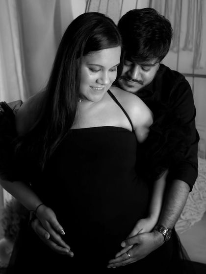 A soft and intimate black and white photo of a couple embracing. The focus is on their hands cradling the baby bump together, symbolizing their shared journey into parenthood.