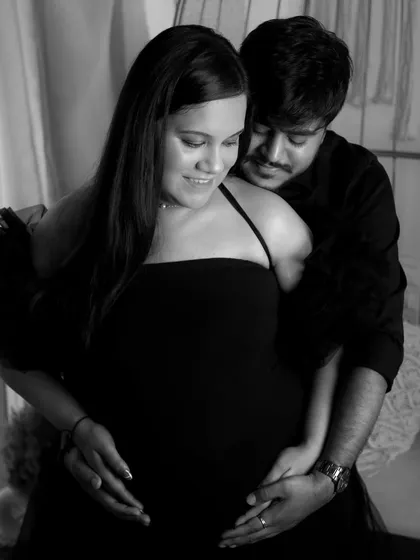 A soft and intimate black and white photo of a couple embracing. The focus is on their hands cradling the baby bump together, symbolizing their shared journey into parenthood.