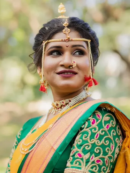 A portrait of a graceful Maharashtrian bride. Her look features a neatly tied bun, traditional gold jewelry, and makeup that highlights her natural elegance against a beautiful outdoor backdrop.