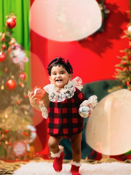 This little one is having a ball, walking with Christmas ornaments in her hands in a vibrant red and green setting.