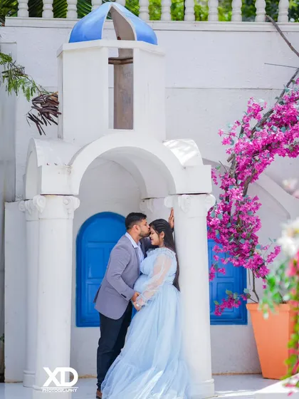 A romantic forehead kiss captured at a beautiful Santorini-style location with pink flowers.