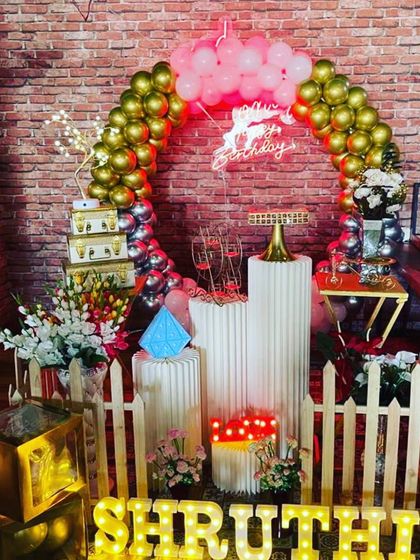 A beautiful setup against a brick wall, showing how I can work with existing venue features. The decor includes a circular balloon arch, a neon sign, and elegant plinths.