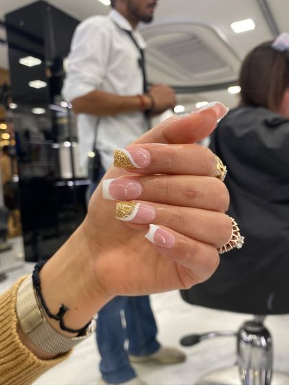 A beautiful French manicure with a twist, featuring a gold glitter accent nail in a wave pattern for a modern and glamorous look.