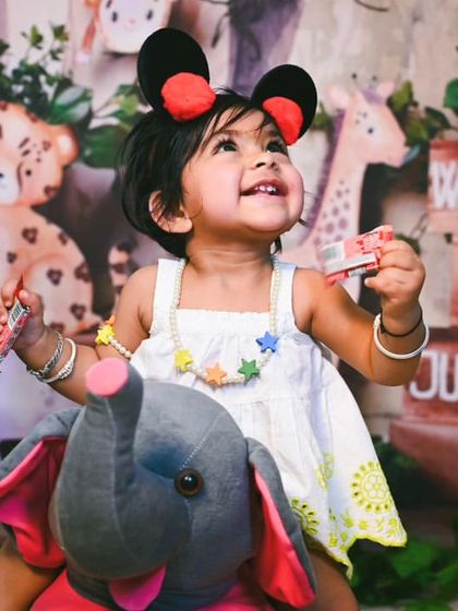 Ready for a jungle adventure, this little one sits on a plush elephant, creating a cute and imaginative scene.