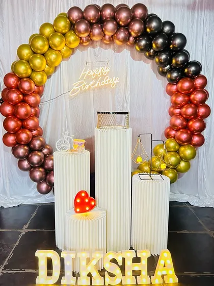 A birthday balloon decoration with a mix of black, gold, and chrome colors. The ribbed stands and marquee letters for 'DIKSHA' complete this elegant setup.