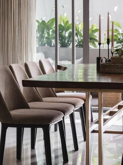 The formal dining area features plush, comfortable chairs and a live-edge wooden table, set against a view of the green planters on the deck.