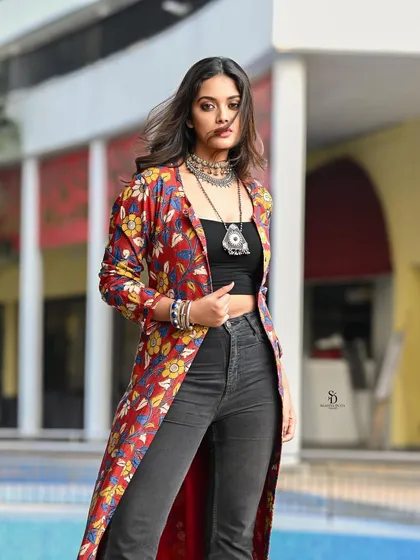 A full-length shot of a model in a bohemian-inspired outfit. The long, floral-print jacket paired with modern silver jewellery creates a stylish, free-spirited look against an urban backdrop.