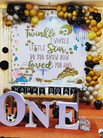 A sweet "Twinkle Twinkle Little Star" theme for a first birthday. The decor features a custom backdrop with the famous rhyme, a black, gold, and silver balloon arch, and large 'ONE' letters for the perfect photo setting.