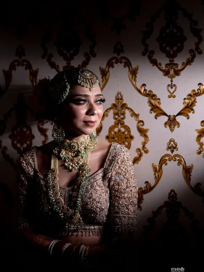 A moment of quiet elegance. The contrast between the dark background and the bride's illuminated face highlights the skillful makeup application and the richness of her traditional attire.