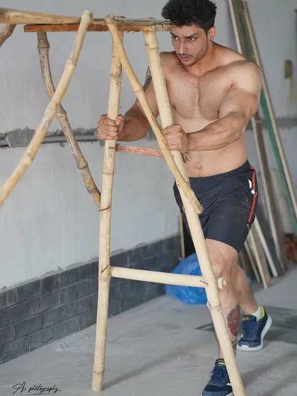 This shot captures the model in a moment of exertion, pushing against a bamboo structure. It emphasizes the power in the arms and chest, telling a story of strength.