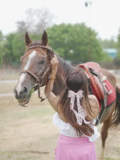 A rider adjusts her horse's bridle while it enjoys a snack. This shows the everyday care and connection at our stables.