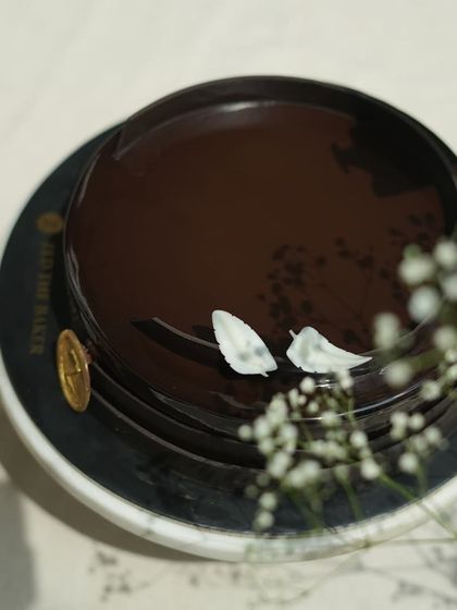 A top-down view of the Belgium Chocolate Cake, adorned with delicate white chocolate leaves and baby's breath. It’s a simple, elegant design that hints at the rich flavor within.