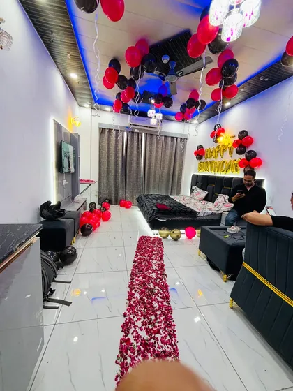 A modern and stylish room decoration for a birthday, featuring a rose petal path, black and red balloons, and dramatic lighting.