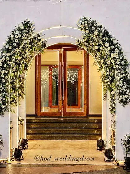 A clean and elegant entrance with minimalist white arches adorned with white flowers, perfect for a chic and modern wedding.
