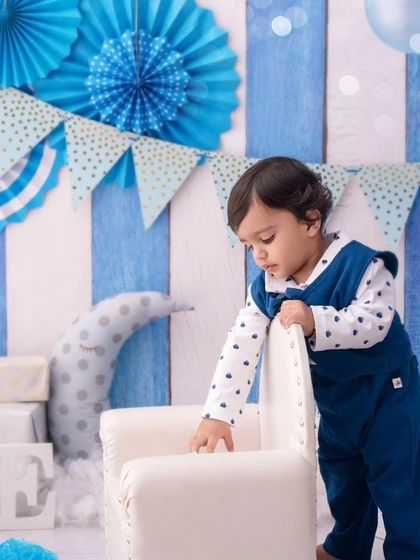 This little boy is exploring his first birthday setup, standing by his chair before the cake smash begins.