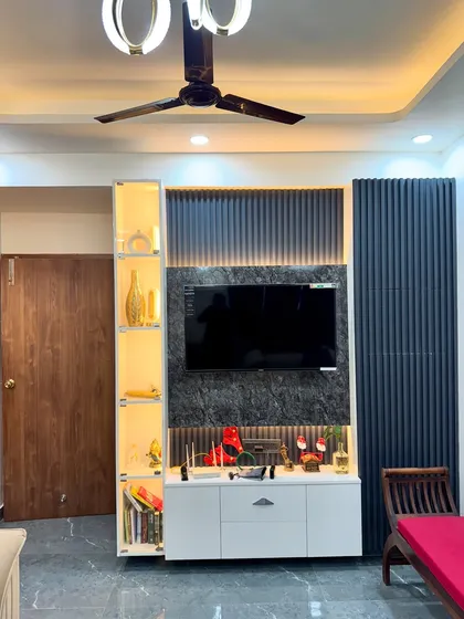 A TV unit design for a project in Amrapali Princly Estate, featuring a dark marble panel, white console, and a lit-up glass display cabinet.