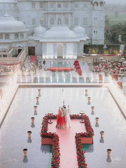 An aerial view of Naomi and Rakshit's varmala ceremony. The couple stands on a platform surrounded by a heart-shaped arrangement of red roses and celebratory cold pyros, creating a truly cinematic moment.