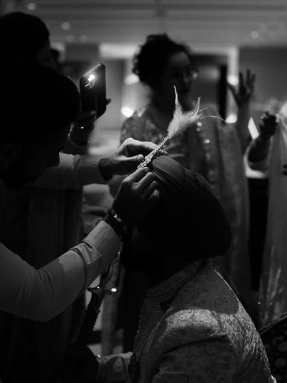 A behind-the-scenes, black and white shot of the groom getting his turban fixed. These candid, unposed moments are just as important as the formal portraits.