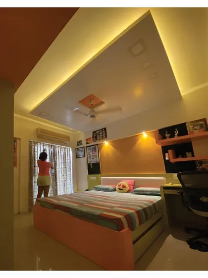 The use of indirect ceiling lighting and focused spotlights above the headboard creates a warm and playful ambiance in this child's room.
