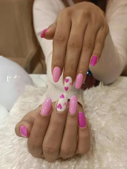A full view of our lovely pink and white heart-themed nail art. This set on long, oval nails is a testament to our ability to create cute and consistent hand-painted designs across all fingers.