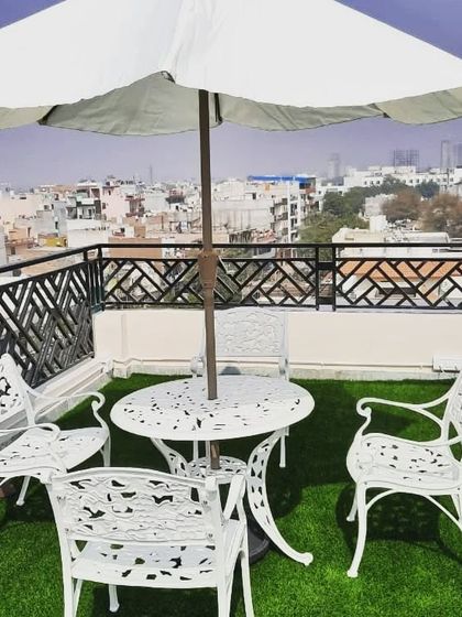 A classic and elegant terrace setup with white cast-aluminum garden furniture and an umbrella, set on a pristine artificial lawn.