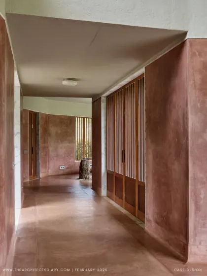 The corridor at Villa Uma is a study in texture and light. The curved, pigmented plaster walls guide you through the space, while slatted wooden screens filter the sunlight and offer glimpses of the garden beyond.