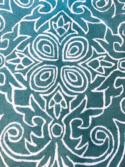 A close-up of a textured carpet featuring a bold, modern interpretation of a classic medallion pattern. The contrast between the raised white lines and the deep teal looped pile creates a dramatic and stylish look.