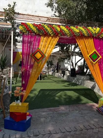 A bright and sunny outdoor entrance for a Haldi or Mehendi function, decorated with yellow and pink drapes and marigold flowers.