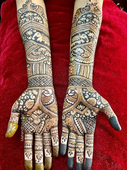 A top-down view of Pooja's bridal mehendi against a rich red background, showing the full scope of the intricate peacock and elephant artwork.