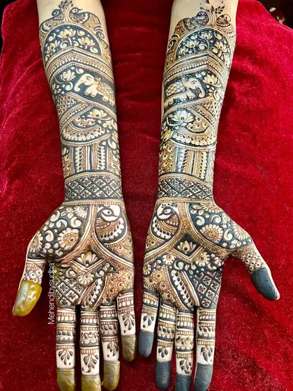 A top-down view of Pooja's bridal mehendi against a rich red background, showing the full scope of the intricate peacock and elephant artwork.