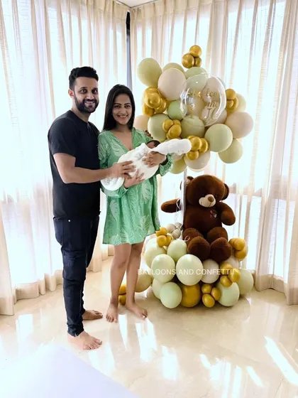 The proud new parents with their little one, posing with the adorable teddy bear welcome home decor I created for them.