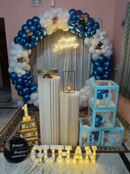 A classic blue and white balloon ring decoration for a boy's birthday, complete with a neon sign, 'B-A-B-Y' blocks, and personalized light-up name.