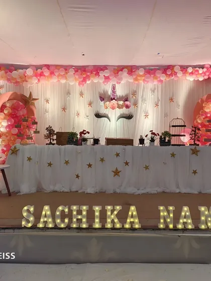 A unicorn themed birthday party setup featuring a beautiful balloon arch in pastel and gold colors. The decor includes a unicorn backdrop, star cutouts, and marquee lights with the child's name.