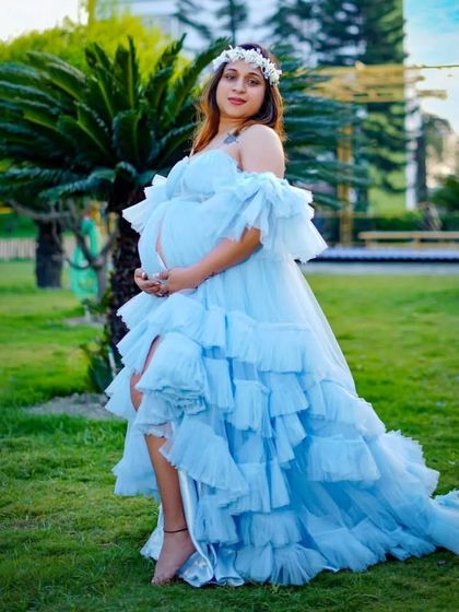A client posing in a lush green park, wearing a light blue high-low ruffled gown. This style is great for showing off your legs and shoes while still having a dramatic train.