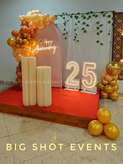 For this 25th anniversary, we designed an elegant stage with a 'Happy Anniversary' neon sign, large light-up marquee numbers, and a stylish balloon arch in a sophisticated gold and peach color scheme.