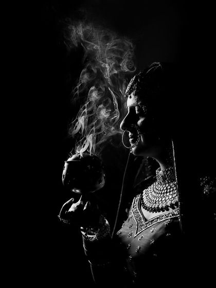 A dramatic black and white portrait of a bride holding a traditional incense burner, with smoke creating a mystical and serene atmosphere.