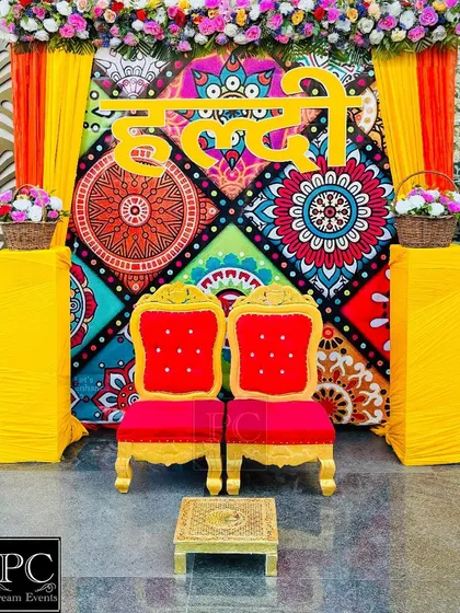 A vibrant and folksy Haldi backdrop. I used a colorful printed fabric panel with the 'Haldi' sign in Hindi, flanked by bright yellow drapes and traditional red and gold chairs.