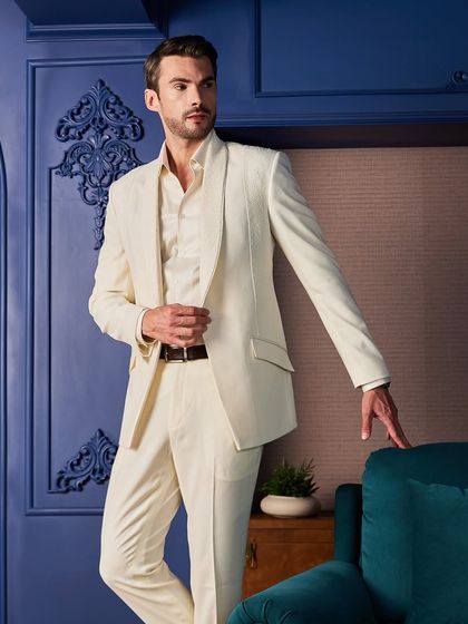 An all-ivory tuxedo offers a fresh and regal alternative to traditional black. This piece features subtle, intricate hand-embroidery with small pearls and beads on the lapel, perfect for a day wedding or a themed celebration.